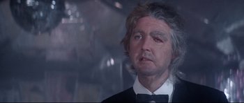 Movie still from “Zardoz” (1974), directed by John Boorman – An older man in a suit and bow tie looking sad; Close Up shot, Low angle