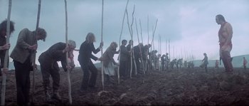 Movie still from “Zardoz” (1974), directed by John Boorman – A group of people standing in the dirt with sticks; Wide shot, High angle