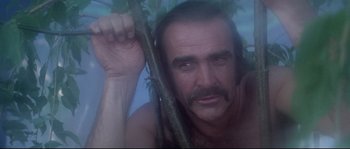 Movie still from “Zardoz” (1974), directed by John Boorman – A man with long hair and a mustache holding onto a tree branch; Close Up shot, Low angle