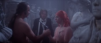 Movie still from “Zardoz” (1974), directed by John Boorman – A man and a woman holding a gun in a room; Medium shot, Over the shoulder angle