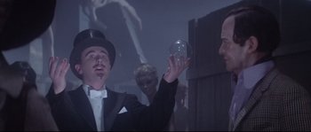 Movie still from “Zardoz” (1974), directed by John Boorman – A man in a top hat holding a crystal ball in front of other people; Medium shot, Low angle