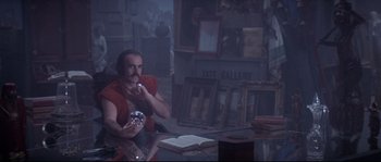 Movie still from “Zardoz” (1974), directed by John Boorman – A man sitting at a table holding a mirror in his hand; Medium shot, High angle