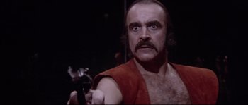 Movie still from “Zardoz” (1974), directed by John Boorman – A man with a beard and mustache is holding a gun; Close Up shot, Low angle