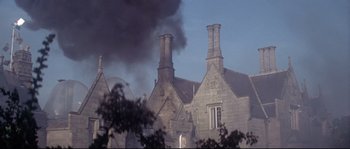 Movie still from “Zardoz” (1974), directed by John Boorman – Smoke billows out of the chimney of an old building; Extreme Wide shot, Low angle
