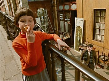 Movie still from “Zazie dans le Métro” (1960), directed by Louis Malle – A little girl eating an apple while standing next to a railing; Wide shot, High angle