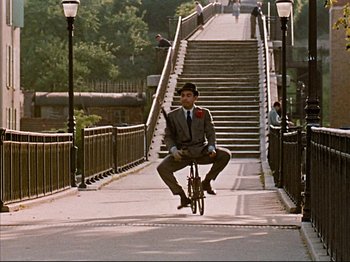Movie still from “Zazie dans le Métro” (1960), directed by Louis Malle – A man riding a bike down the side of a bridge; Wide shot, High angle