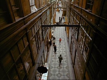 Movie still from “Zazie dans le Métro” (1960), directed by Louis Malle – People are walking down a long hallway in a building; Extreme Wide shot, High angle