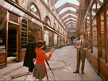 Movie still from “Zazie dans le Métro” (1960), directed by Louis Malle – A man and a woman are standing in an arcade; Wide shot, High angle