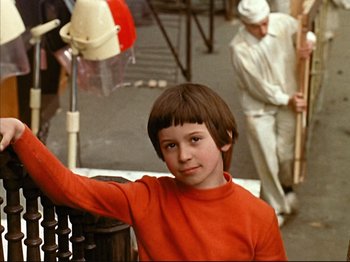 Movie still from “Zazie dans le Métro” (1960), directed by Louis Malle – A young boy in a red shirt is standing in front of a crowd; Medium shot, High angle