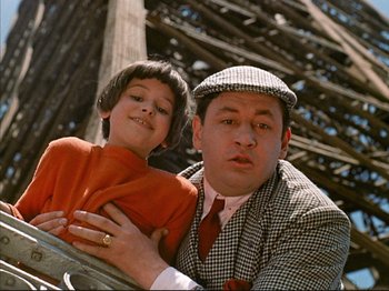 Movie still from “Zazie dans le Métro” (1960), directed by Louis Malle – A man and a boy posing for a picture in front of a wooden structure; Close Up shot, Low angle