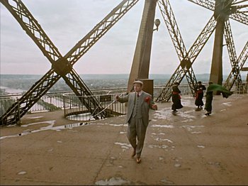Movie still from “Zazie dans le Métro” (1960), directed by Louis Malle – A man in a suit and hat standing in front of a bridge; Extreme Wide shot, High angle