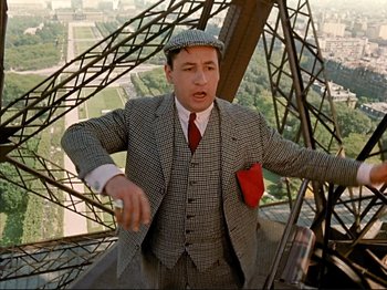 Movie still from “Zazie dans le Métro” (1960), directed by Louis Malle – A man in a suit and tie standing on a metal structure; Medium shot, Low angle