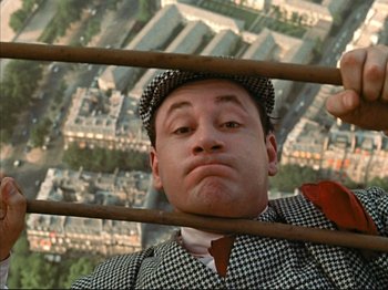 Movie still from “Zazie dans le Métro” (1960), directed by Louis Malle – A man in a suit and hat holding onto a wooden pole; Close Up shot, Overhead angle