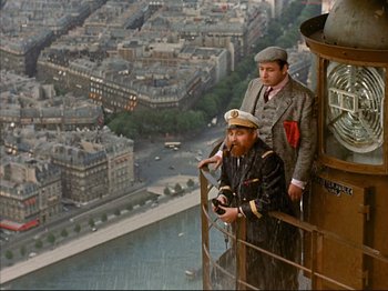 Movie still from “Zazie dans le Métro” (1960), directed by Louis Malle – Two men standing on the side of a building looking out over a city; Wide shot, High angle