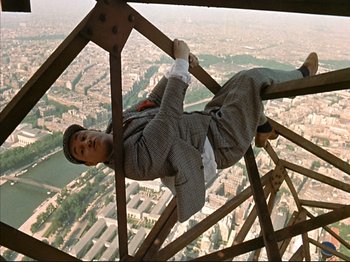 Movie still from “Zazie dans le Métro” (1960), directed by Louis Malle – A man in a suit hanging from a metal structure; Wide shot, Overhead angle