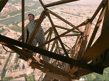 Movie still from “Zazie dans le Métro” (1960), directed by Louis Malle – A man standing on top of a metal structure; Wide shot, Low angle