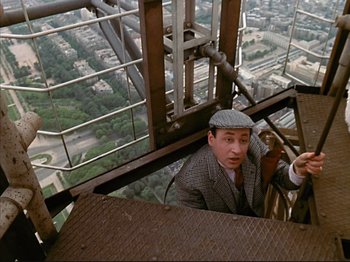 Movie still from “Zazie dans le Métro” (1960), directed by Louis Malle – A man in a suit and a hat standing on a balcony; Medium shot, Overhead angle