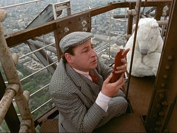 Movie still from “Zazie dans le Métro” (1960), directed by Louis Malle – A man sitting on top of a building looking at his cell phone; Medium shot, Low angle