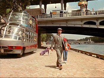 Movie still from “Zazie dans le Métro” (1960), directed by Louis Malle – A man in a suit and hat walking by a double decker bus; Wide shot, Low angle