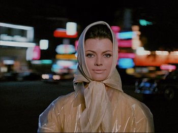Movie still from “Zazie dans le Métro” (1960), directed by Louis Malle – A woman wearing a head scarf and a plastic raincoat; Close Up shot, Low angle