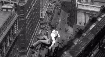Movie still from “Zelig” (1983), directed by Woody Allen – A man sitting on top of a chair on top of a building; Wide shot, Overhead angle