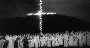 Movie still from “Zelig” (1983), directed by Woody Allen – A large group of people wearing white robes and holding up their hands in front of a cross; Extreme Wide shot, High angle