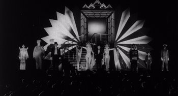 Movie still from “Zelig” (1983), directed by Woody Allen – A black and white photo of a group of people on stage; Wide shot, Low angle