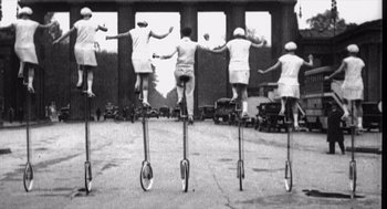 Movie still from “Zelig” (1983), directed by Woody Allen – A black and white photo of a group of people riding on top of a bicycle; Wide shot, Low angle