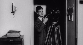 Movie still from “Zelig” (1983), directed by Woody Allen – A black and white photo of a man in a suit and tie standing in front of a camera; Medium shot, Low angle