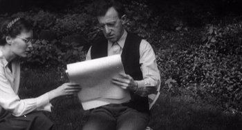 Movie still from “Zelig” (1983), directed by Woody Allen – A black and white photo of a man sitting on the grass reading a piece of paper; Medium shot, Over the shoulder angle