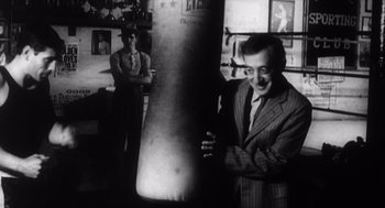 Movie still from “Zelig” (1983), directed by Woody Allen – A man standing next to a punching bag in a room; Medium shot, Low angle