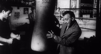 Movie still from “Zelig” (1983), directed by Woody Allen – An old photo of a man in a suit and a boxing bag; Medium shot, High angle