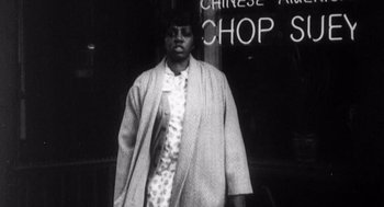 Movie still from “Zelig” (1983), directed by Woody Allen – A black and white photo of a man in a suit and tie standing in front of a chop shop sign; Medium shot, Low angle