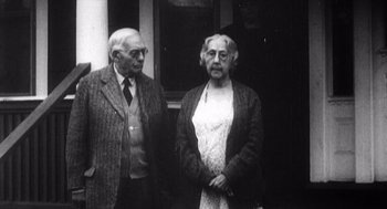 Movie still from “Zelig” (1983), directed by Woody Allen – An older man standing next to an older woman in front of a building; Medium shot, Over the shoulder angle