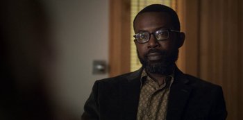 Movie still from “Archive 81” (2022), created by Rebecca Sonnenshine – A man with a beard wearing glasses and a suit; Close Up shot, Over the shoulder angle