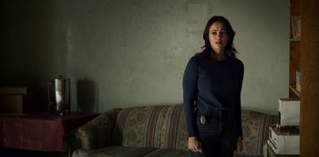 Movie still from “Archive 81” (2022), created by Rebecca Sonnenshine – A woman standing in front of a couch in a living room; Medium shot, Low angle