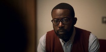 Movie still from “Archive 81” (2022), created by Rebecca Sonnenshine – A man wearing glasses and a sweater vest looks at the camera; Close Up shot, Over the shoulder angle