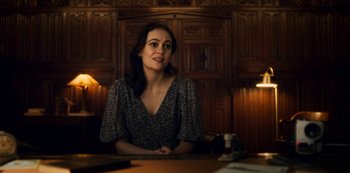 Movie still from “Archive 81” (2022), created by Rebecca Sonnenshine – A woman sitting at a table in front of a wooden wall; Medium shot, Over the shoulder angle