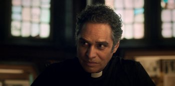 Movie still from “Archive 81” (2022), created by Rebecca Sonnenshine – A man in a priest's outfit is looking at the camera; Close Up shot, Over the shoulder angle