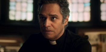 Movie still from “Archive 81” (2022), created by Rebecca Sonnenshine – A man in a priest's outfit stares into the camera; Close Up shot, Low angle