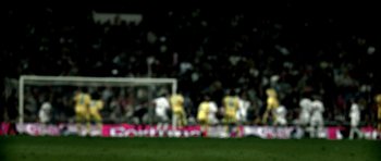 Movie still from “Zidane: A 21st Century Portrait” (2006), directed by Philippe Parreno – A group of men playing a game of soccer on a field; Wide shot, Over the shoulder angle