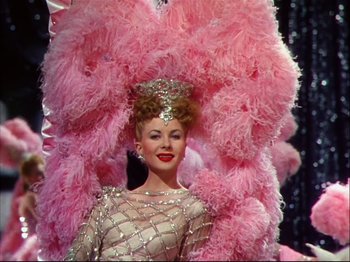 Movie still from “Ziegfeld Follies” (1945), directed by Roy Del Ruth – A woman in a costume with pink feathers on her head; Medium shot, Low angle