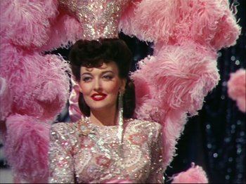 Movie still from “Ziegfeld Follies” (1945), directed by Roy Del Ruth – A woman in a pink dress and a pink and white feathered headdress; Medium shot, Low angle
