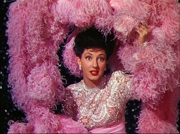 Movie still from “Ziegfeld Follies” (1945), directed by Roy Del Ruth – A woman in a pink dress and a pink feather boa; Medium shot, Low angle