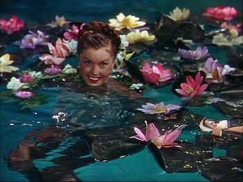 Movie still from “Ziegfeld Follies” (1945), directed by Roy Del Ruth – A woman swimming in a body of water surrounded by water lilies; Medium shot, High angle