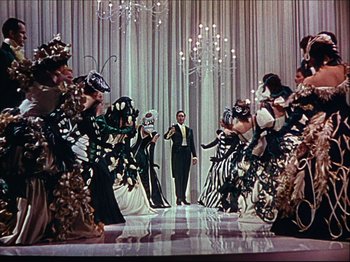 Movie still from “Ziegfeld Follies” (1945), directed by Roy Del Ruth – A man standing in front of a group of people in costumes; Wide shot, Low angle