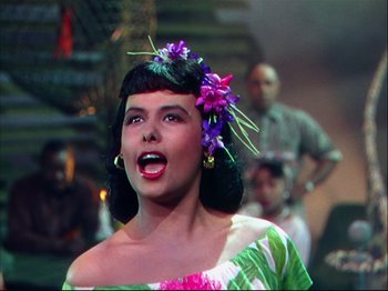 Movie still from “Ziegfeld Follies” (1945), directed by Roy Del Ruth – A woman with a flower in her hair singing in front of a crowd; Close Up shot, Low angle