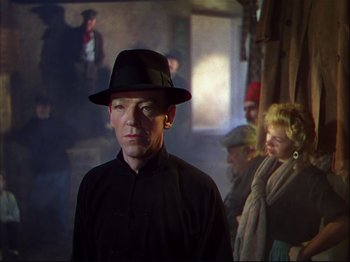 Movie still from “Ziegfeld Follies” (1945), directed by Roy Del Ruth – A man wearing a black hat standing next to other people; Medium shot, Over the shoulder angle