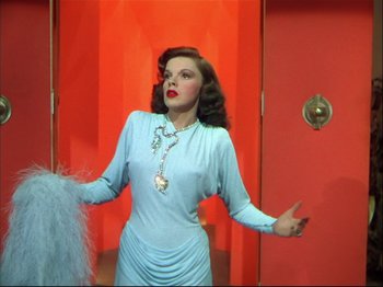 Movie still from “Ziegfeld Follies” (1945), directed by Roy Del Ruth – A beautiful woman in a blue dress standing in front of a door; Medium shot, Low angle