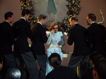 Movie still from “Ziegfeld Follies” (1945), directed by Roy Del Ruth – A group of men standing around a woman in front of a mirror; Wide shot, Low angle
